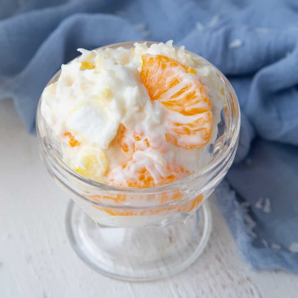 glass parfait dish of ambrosia (5 cup salad) next to a blue tea towel.