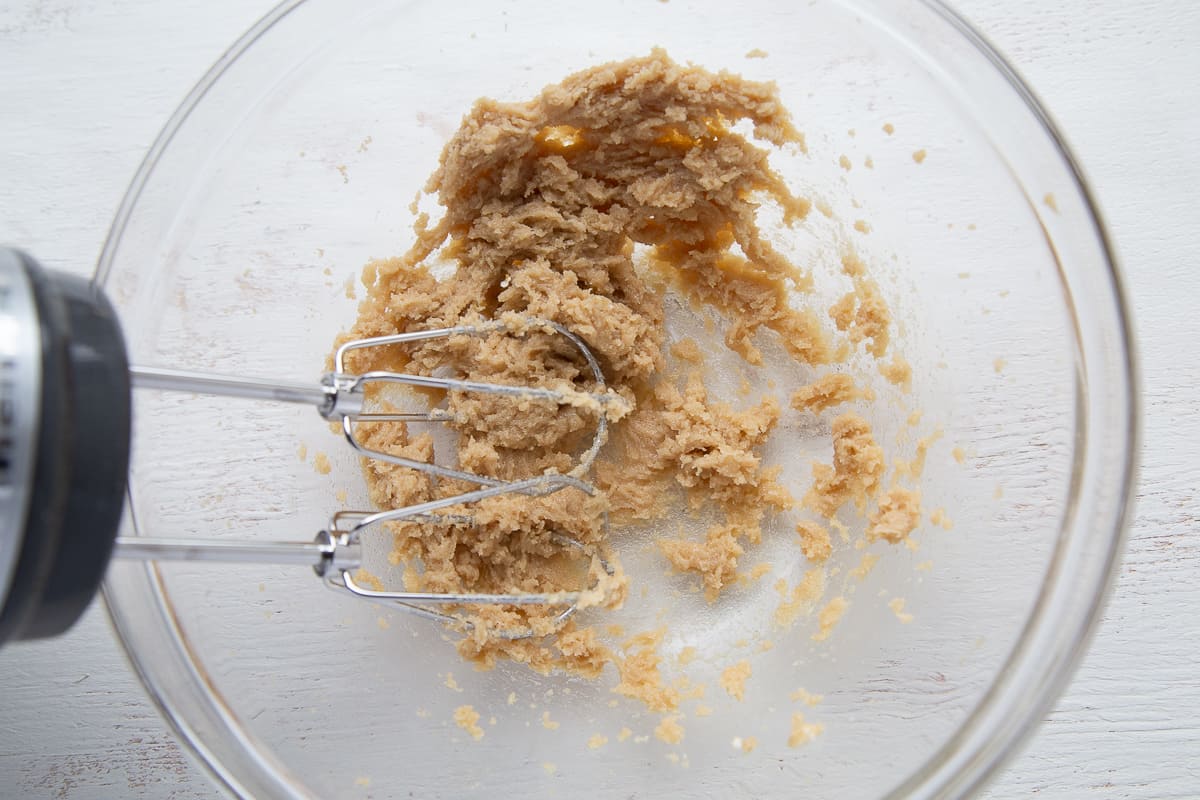 glass bowl with butter and brown sugar, with a handheld mixer sticking out.