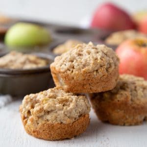 three apple muffins stacked on top of each other, with a muffin tin in the background.