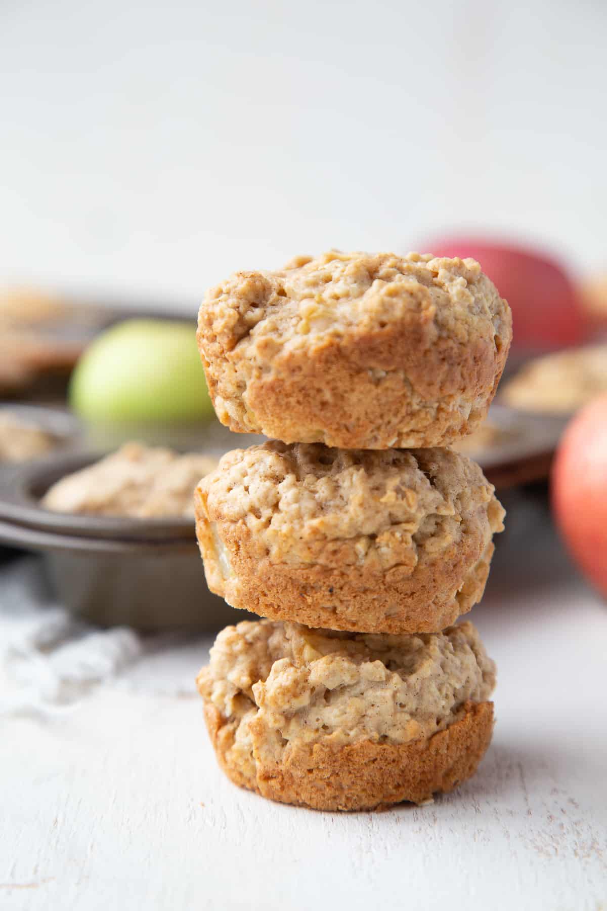 three apple muffins stacked on top of each other, with a muffin tin in the background.