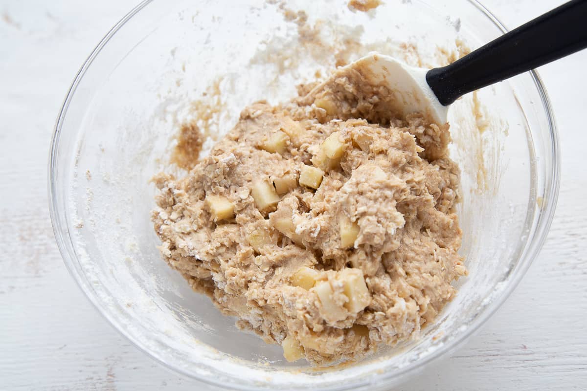 muffin batter with apples in a glass bowl with a spatula sticking out.