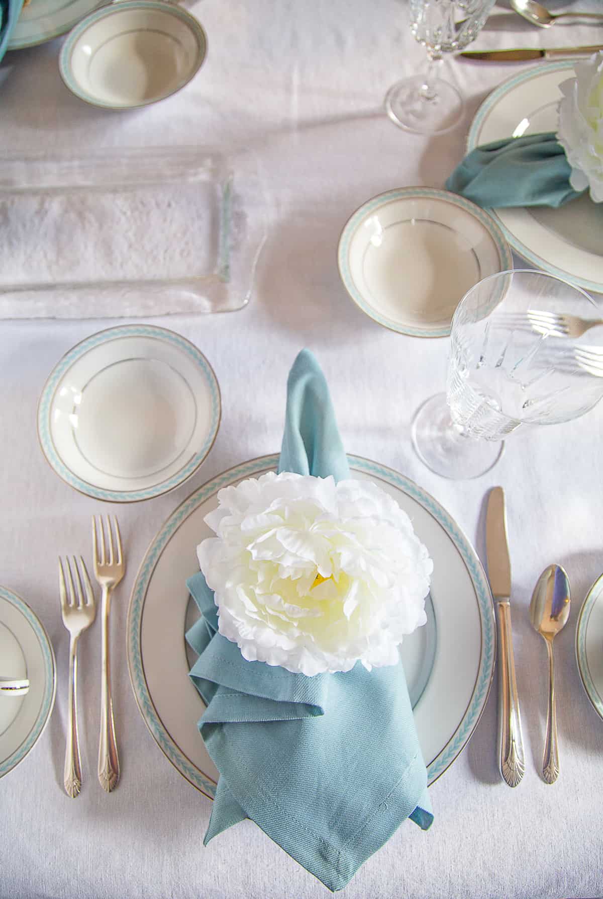 table set with china, blue napkins, and peony napkin rings.