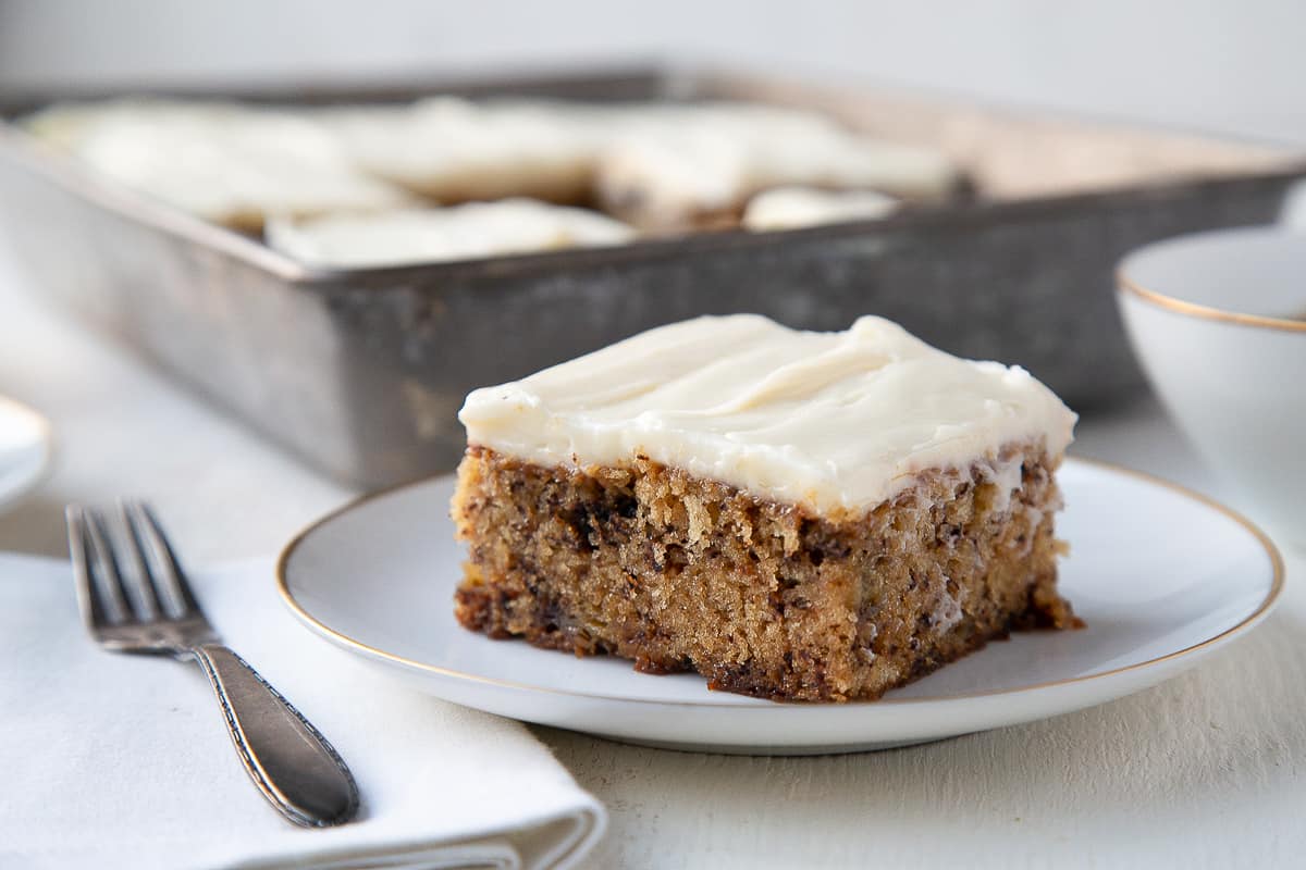 slice of banana cake on a white plate next to a fork and white napkin.