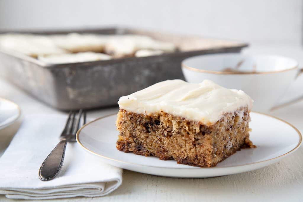 slice of banana cake with walnuts inside, topped with cream cheese frosting.