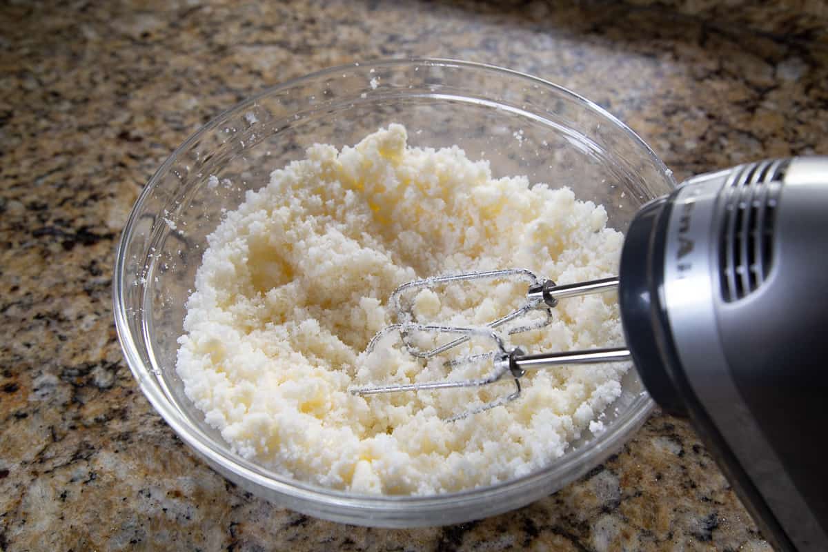 handheld mixer mixing butter and sugar in a glass bowl.