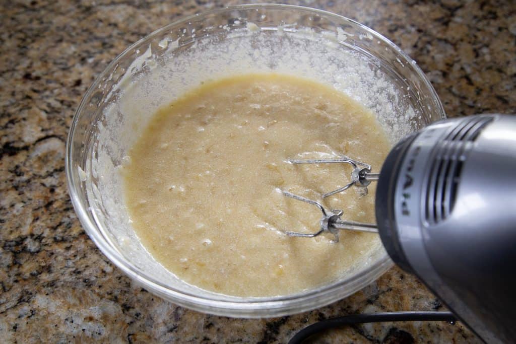 handheld mixer mixing sugar, butter, and eggs in a glass bowl.