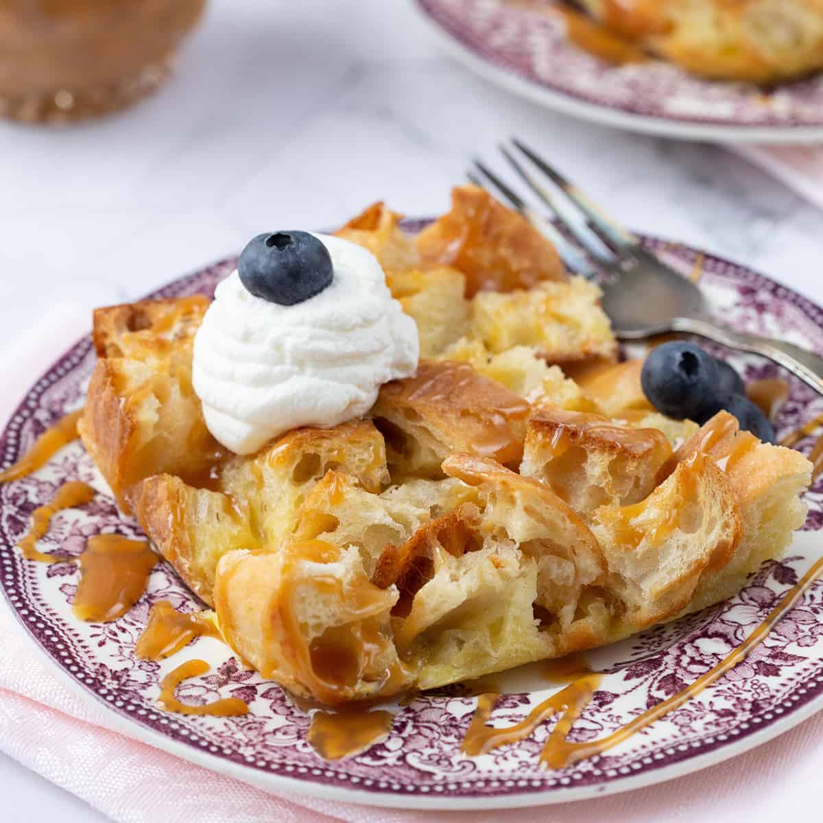 bread pudding on a purple patterned plate, topped with whipped cream and blueberries.