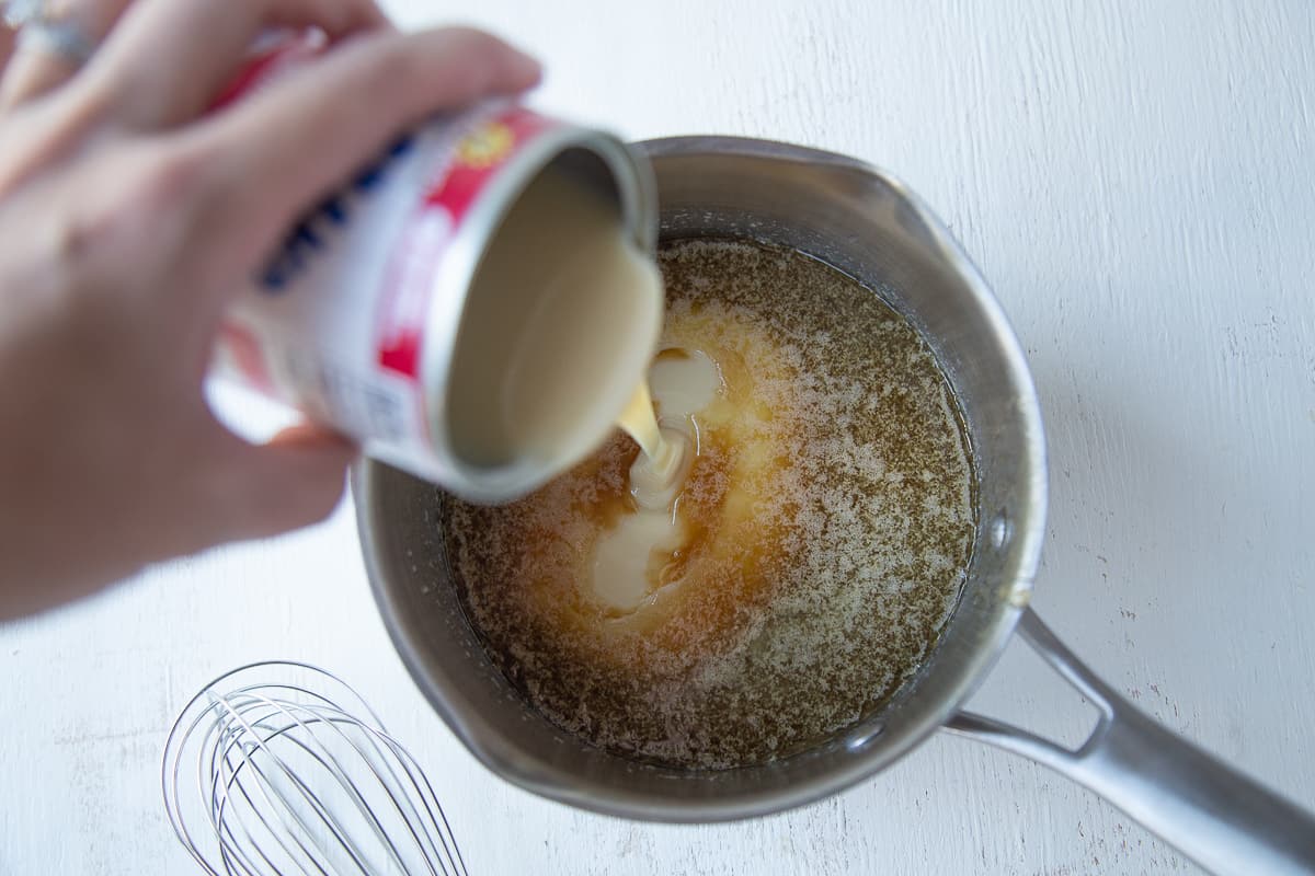 hand pouring sweetened condensed milk into a saucepan.
