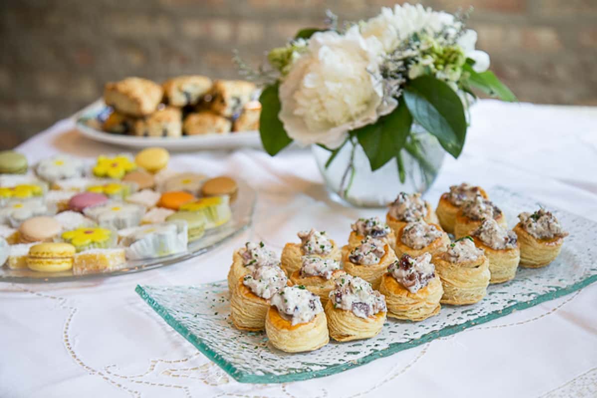 chicken salad in puff pastry cups on a glass serving platter on a buffet table with white flowers.