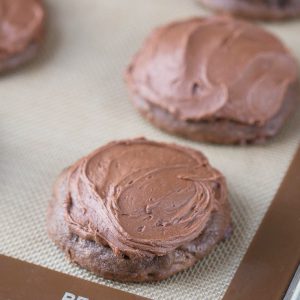chocolate cookies with chocolate frosting on a silicone baking mat.
