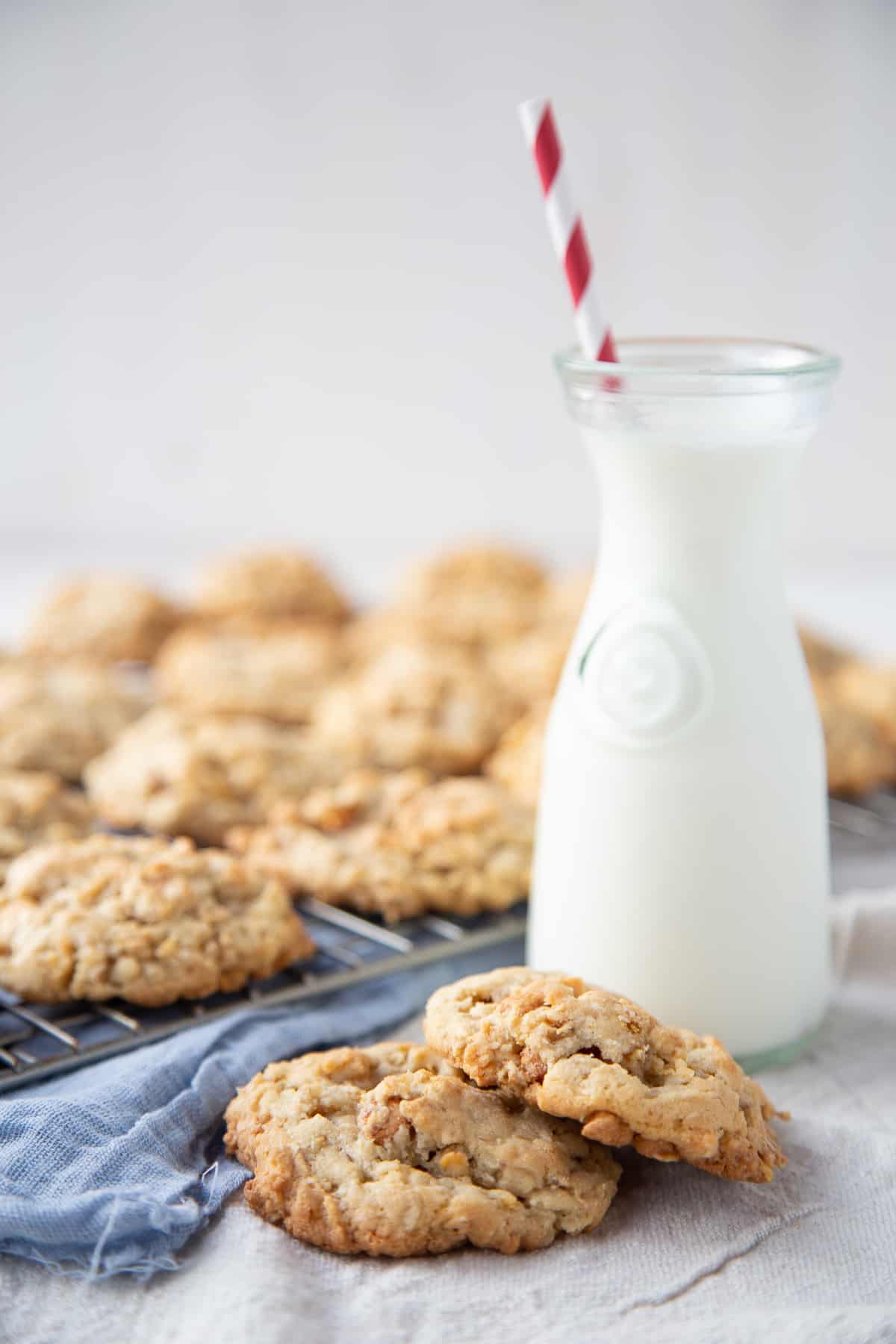 corn flake cookies on a white table with a glass of milk and a blue tea towel.