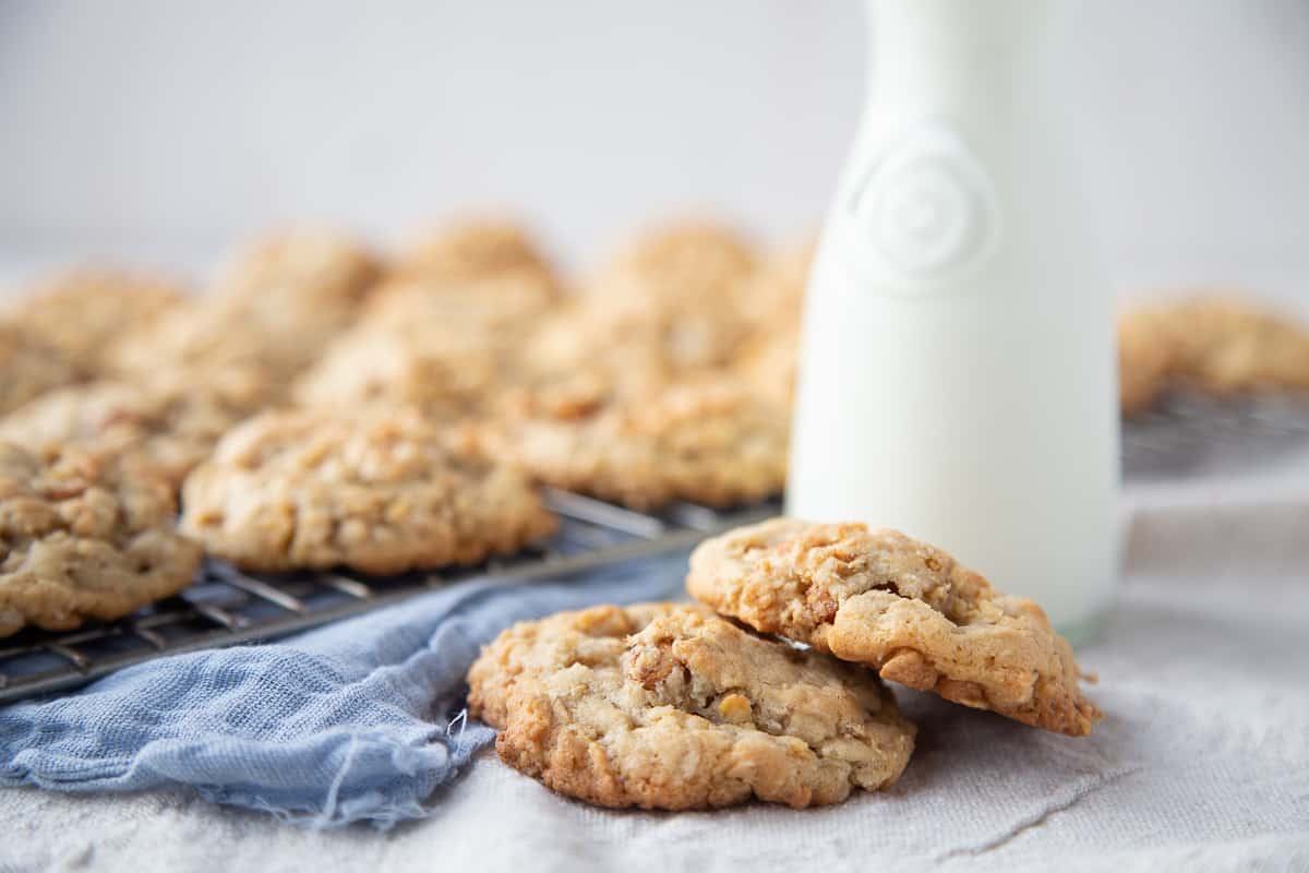 corn flake cookies on a white table with a glass of milk and a blue tea towel.