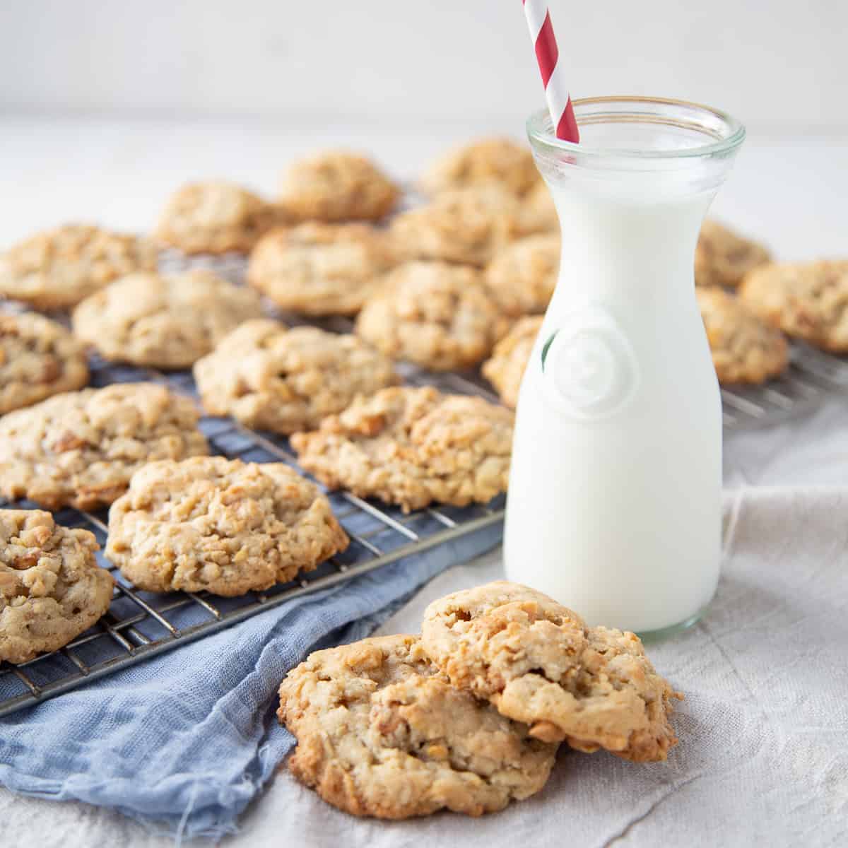 corn flake cookies on a white table with a glass of milk and a blue tea towel.