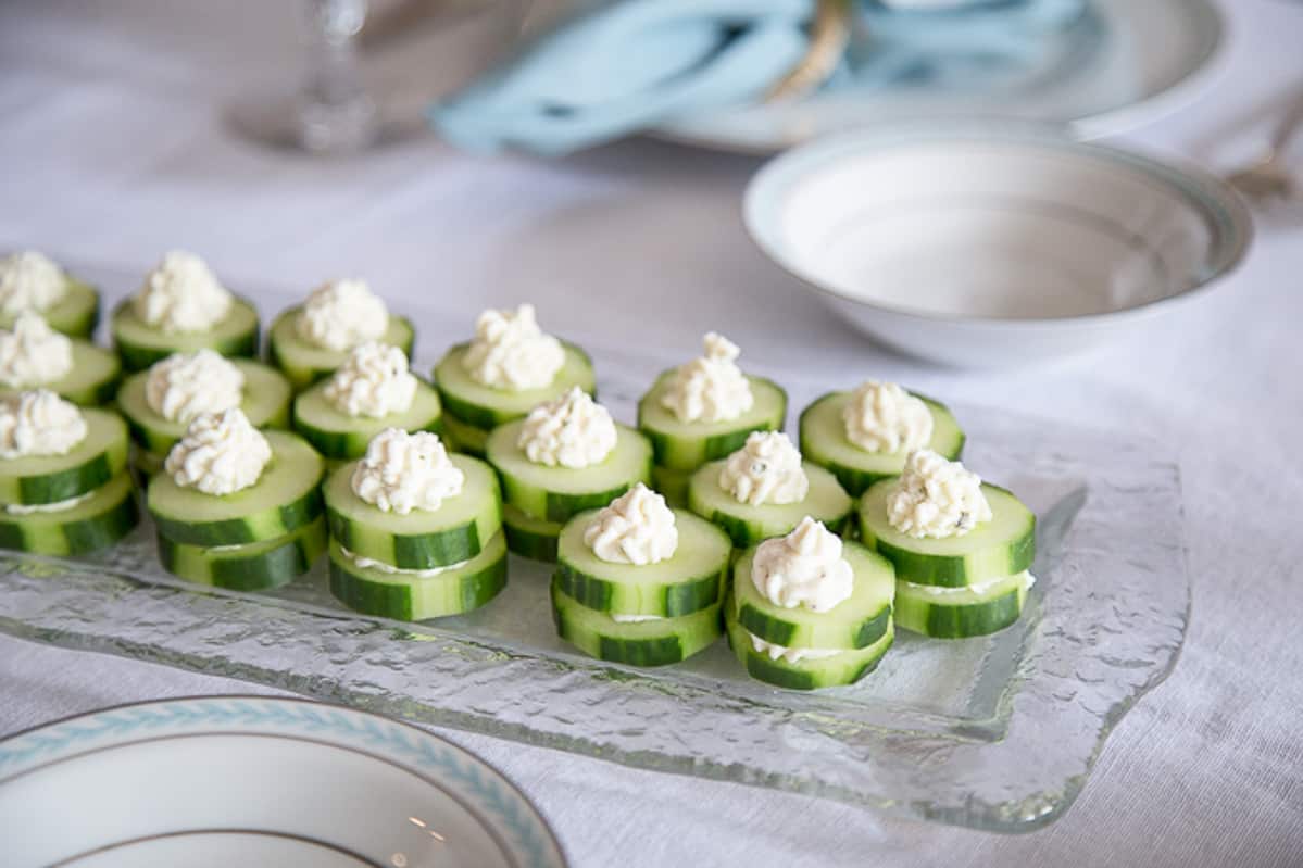 cucumber round appetizers with piped boursin cheese on a glass serving platter.