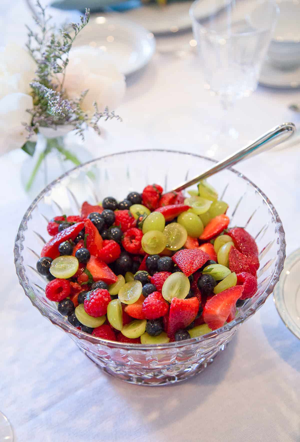 fruit salad in a glass bowl on a white tablecloth.