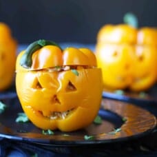 orange bell peppers carved into a jack o lantern on a black plate.