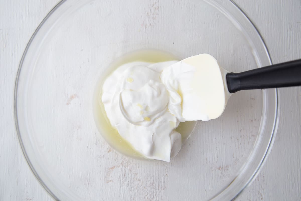 pineapple juice and sour cream in a large glass bowl with a spatula.