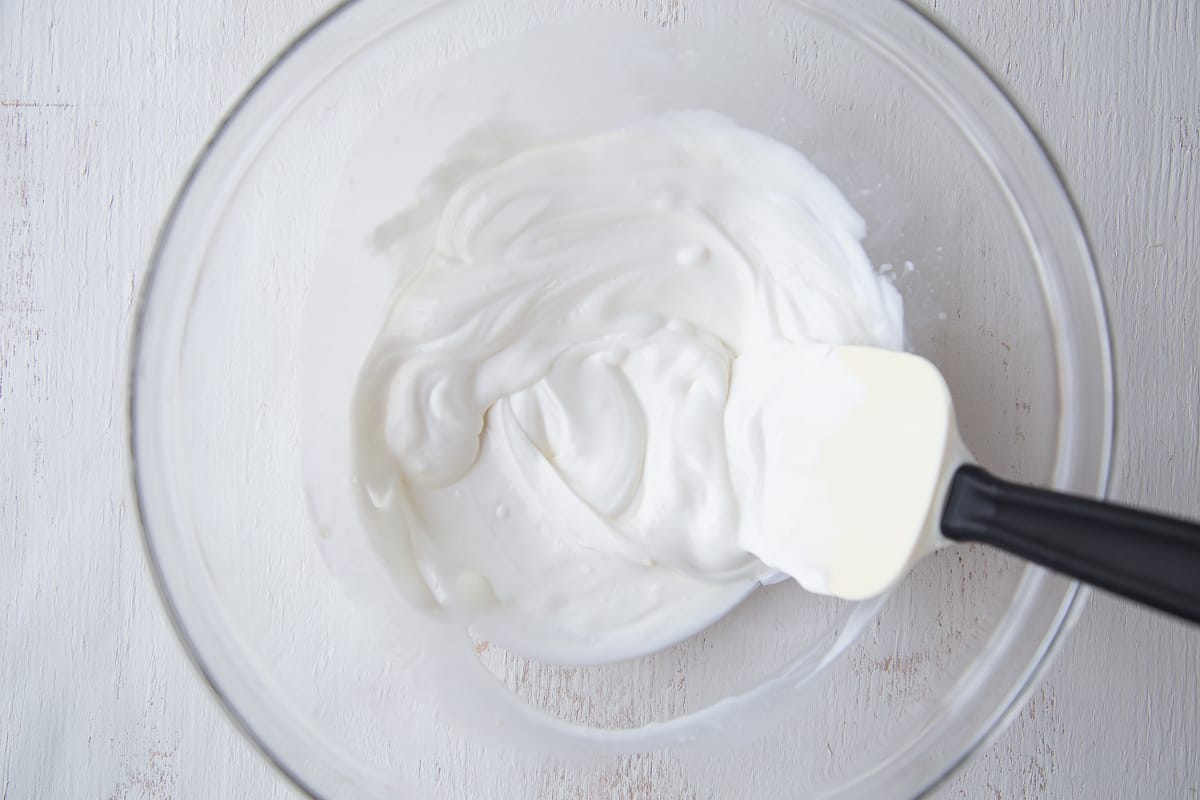 pineapple juice and sour cream stirred together in a large glass bowl with a spatula.