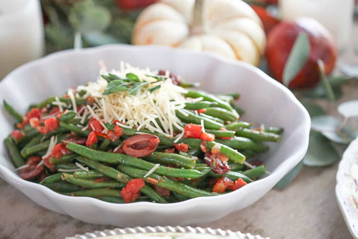 italian green beans in a scalloped white dish on a table with pumpkins and leaves.