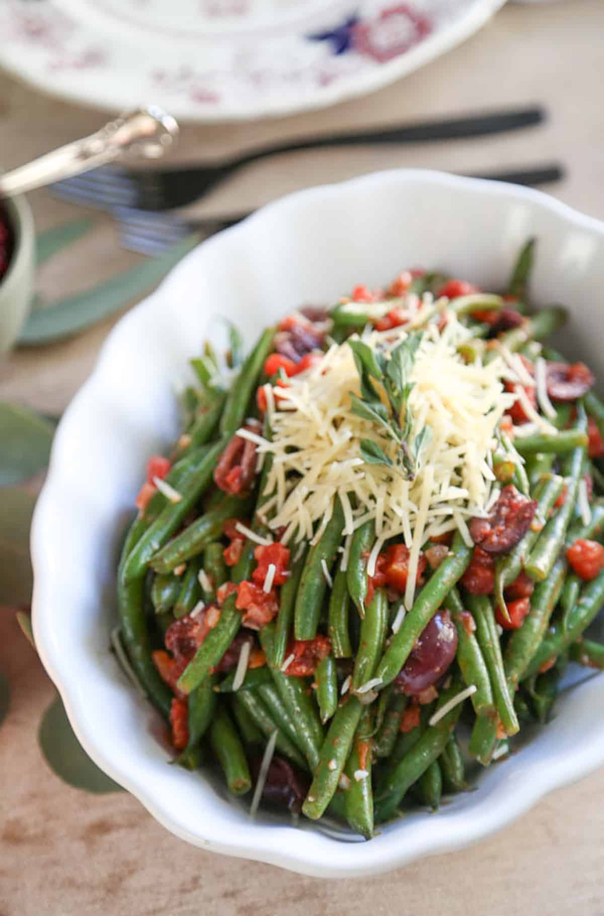 italian green beans in a white scalloped dish on a beige tablecloth.