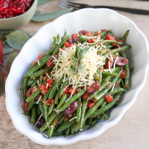 Italian green beans in a white scalloped dish on a beige tablecloth.