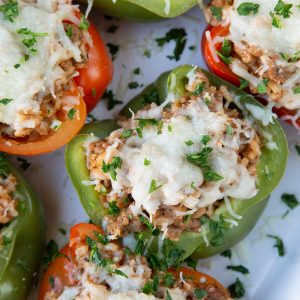 italian stuffed peppers topped with cheese in a white casserole dish.