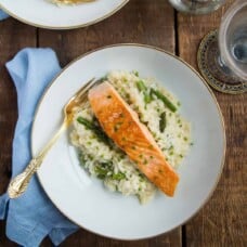 salmon over risotto on white china, sitting on a wooden table.