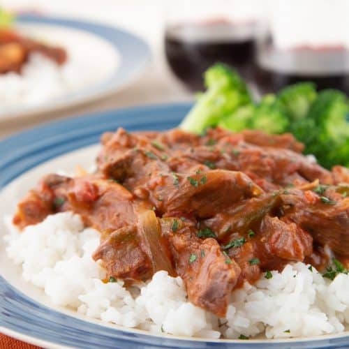 smothered steak on top of rice with broccoli and red wine in the background.