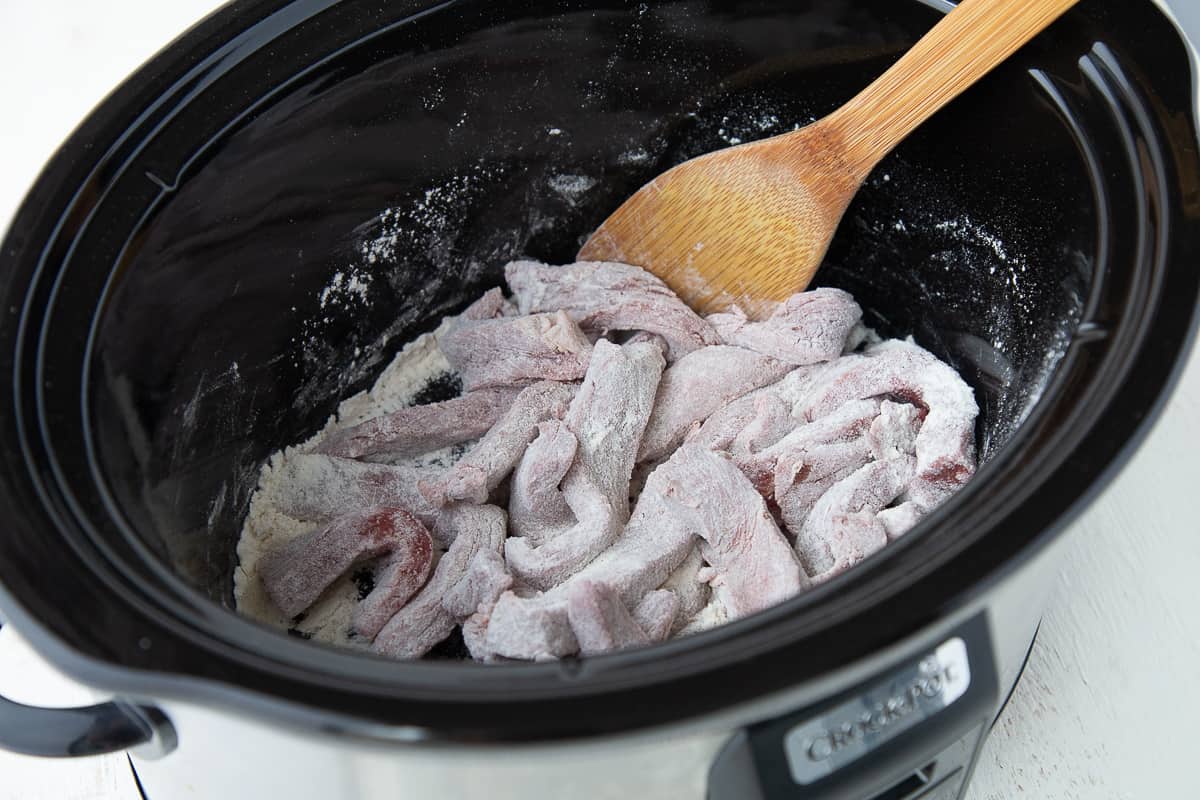 flour coated steak in a slow cooker.