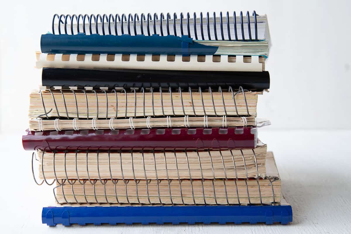 stack of wire bound vintage cookbooks on a white table.