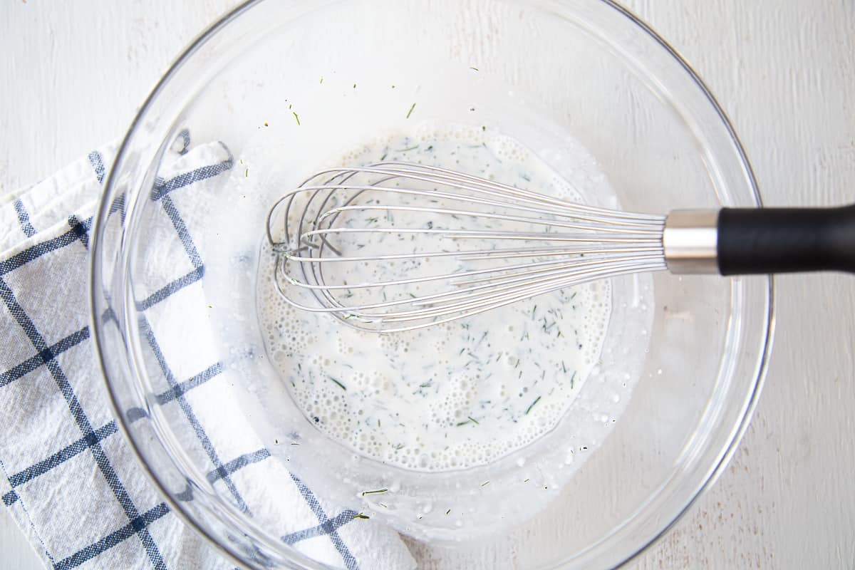 creamy dill dressing being whisked in a large glass bowl.