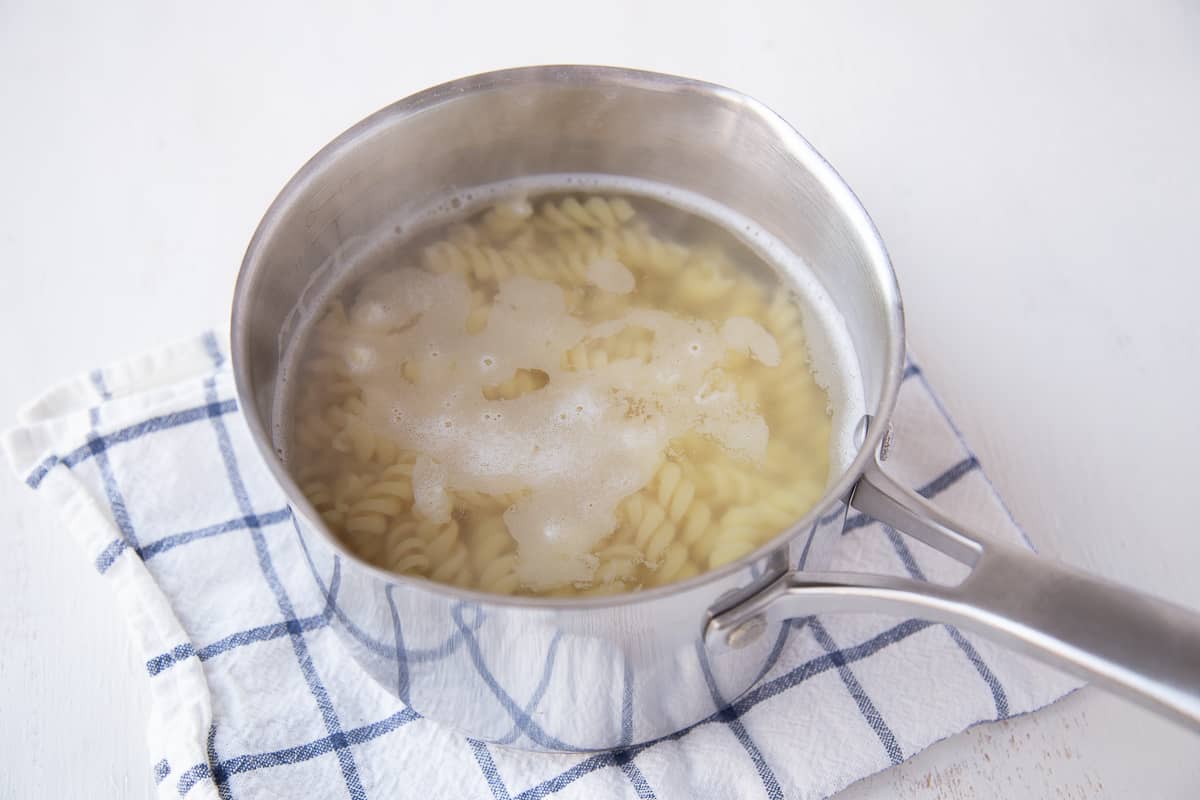 pasta cooking in a saucepan, sitting on a blue and white tea towel.