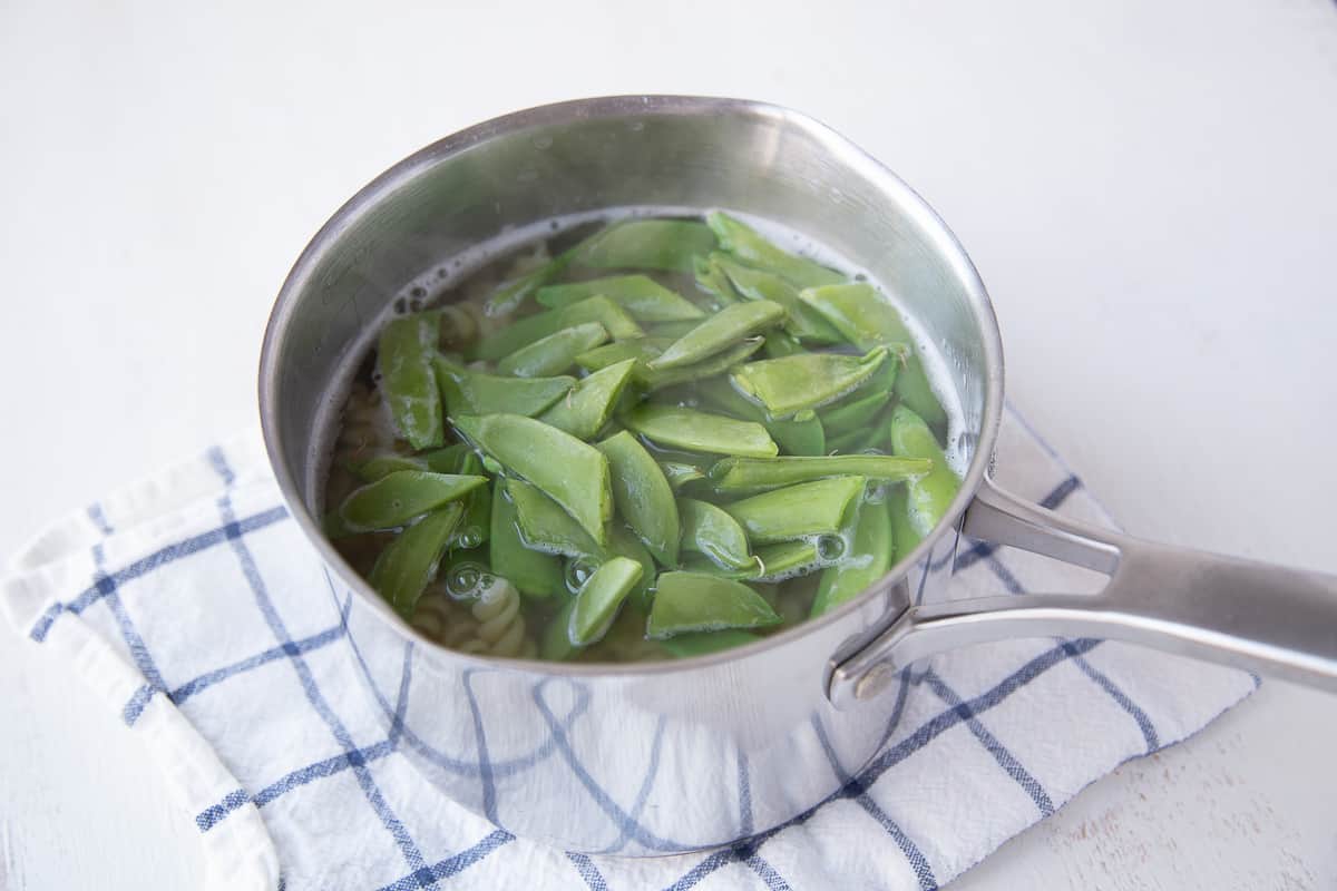 pasta and snap peas in boiling water in a saucepan.