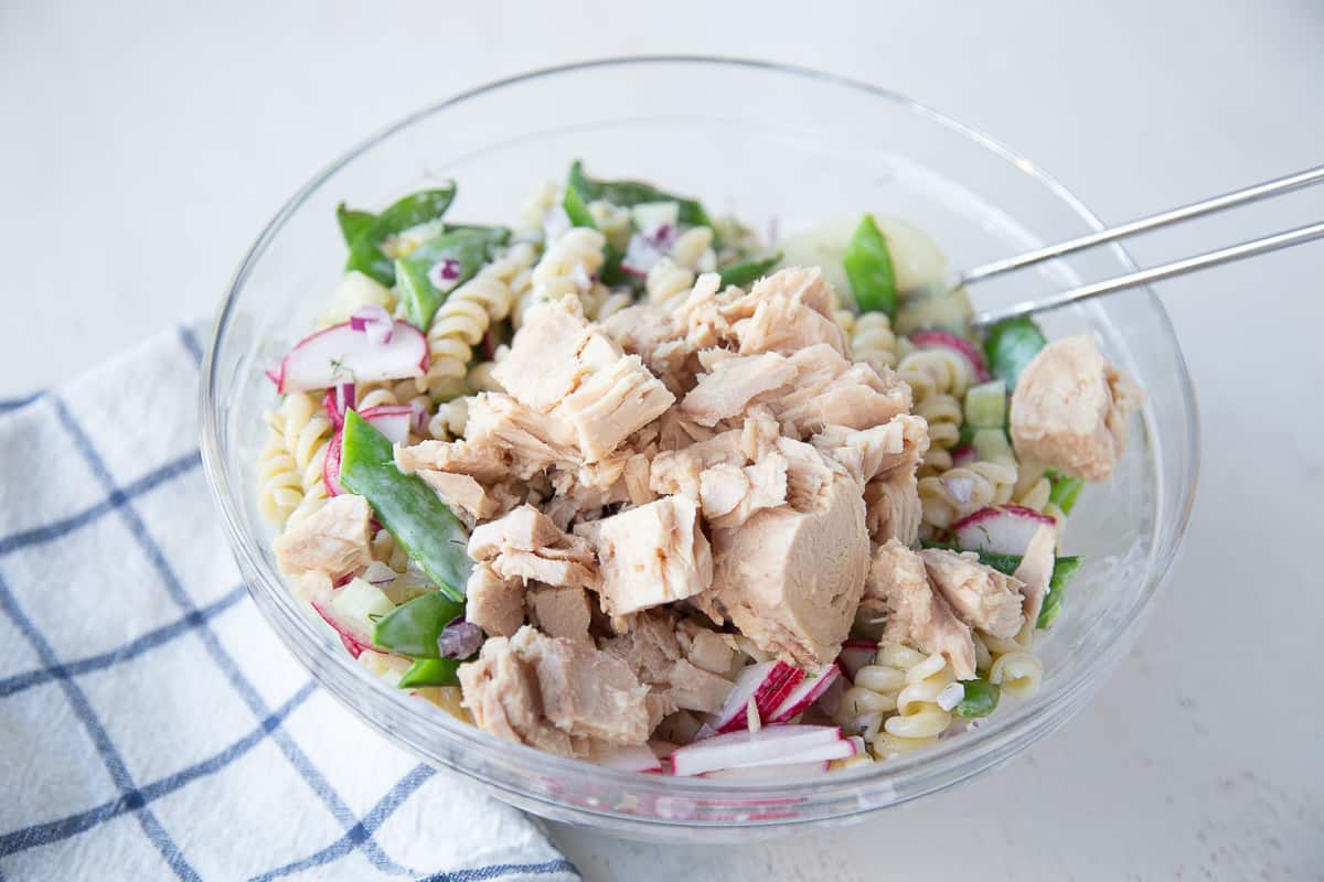 glass bowl filled with tuna pasta salad ingredients, with tuna on top.