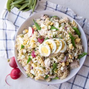 white bowl filled with tuna pasta salad sitting on a white and blue tea towel.