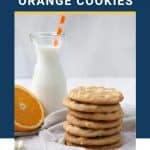 stack of white chocolate chip cookies with a glass of milk and half an orange.
