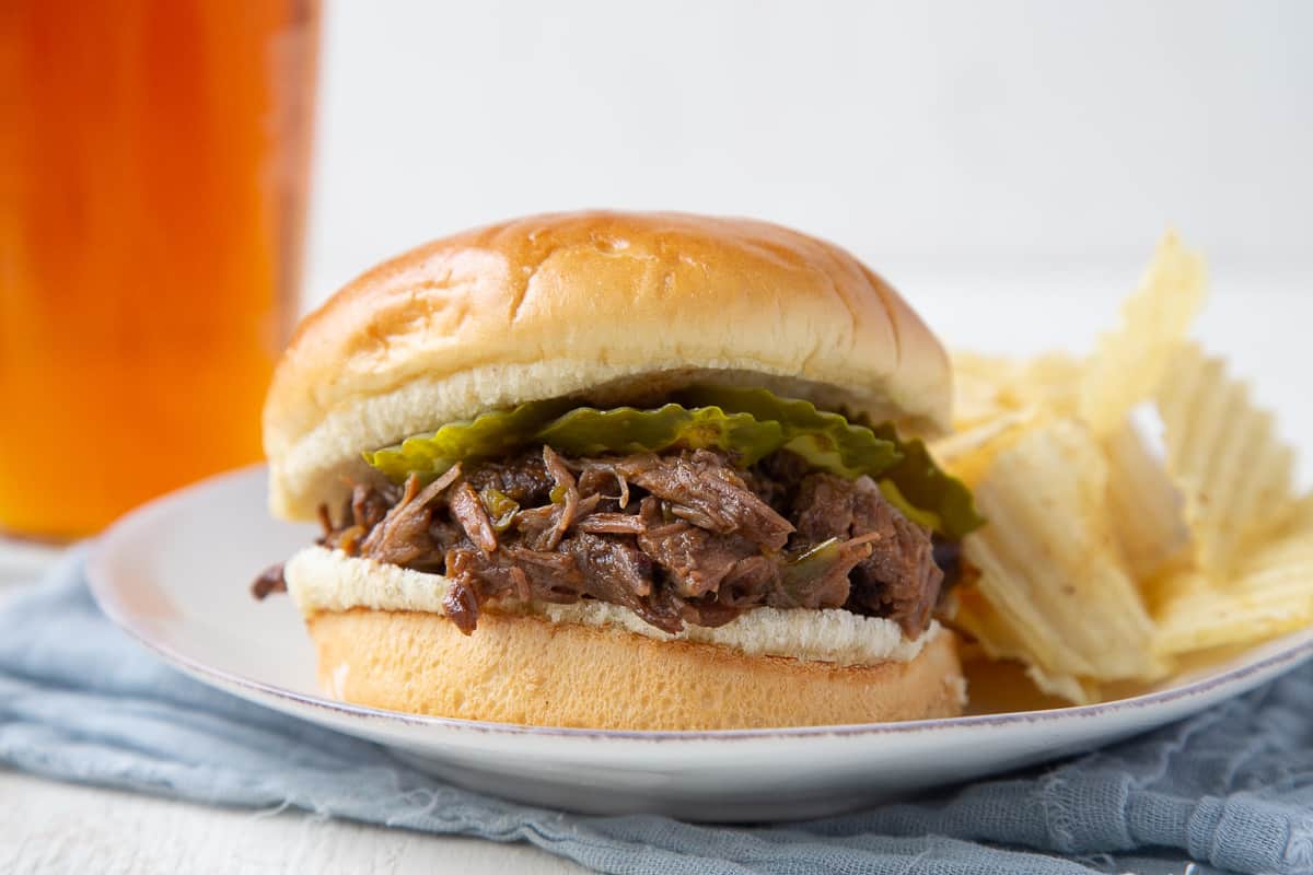 beef bbq sandwich on a white plate with chips and a pint of beer.