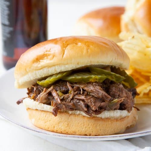 shredded beef with pickles on a brioche bun on a white plate.