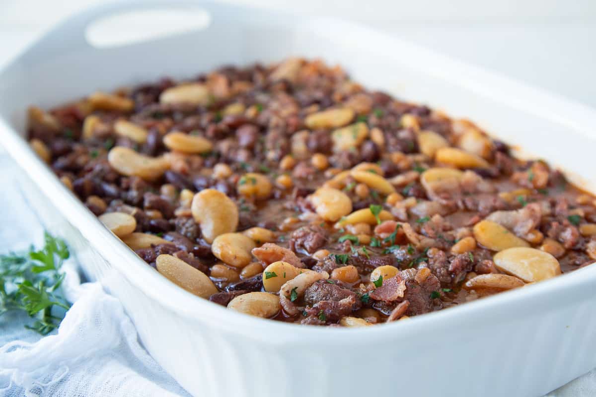 side view of baked beans in a white casserole dish with parsley on the side.