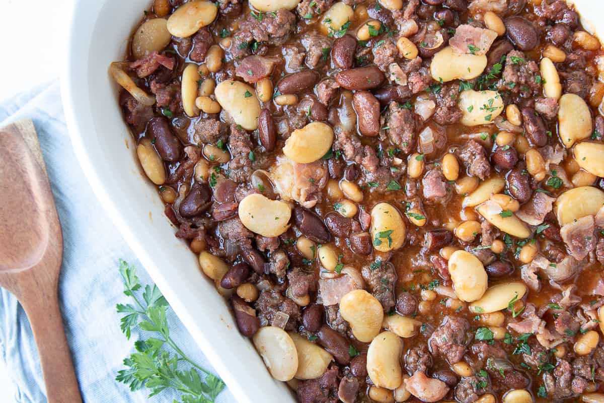calico baked beans in a white casserole dish with a wooden spoon on the side.