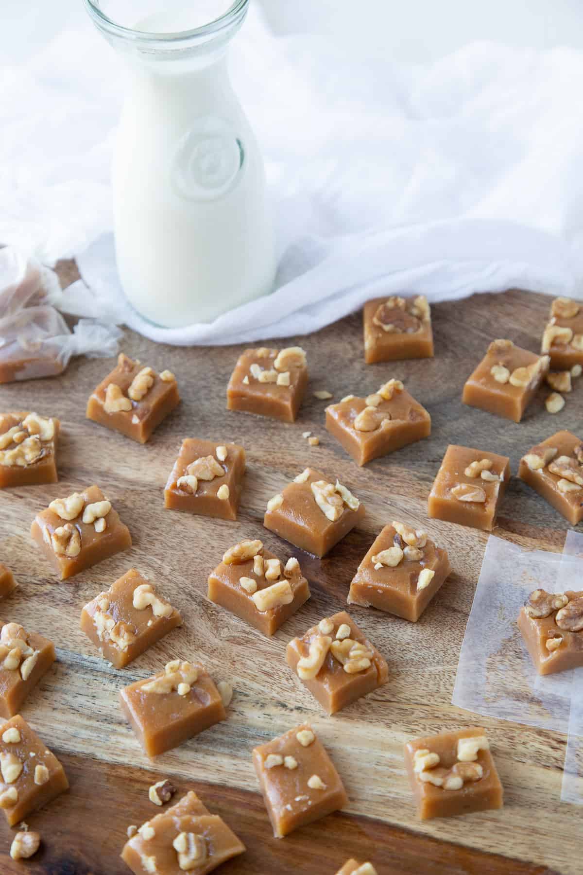 walnut caramels on a wooden board with a glass jug of milk nearby.