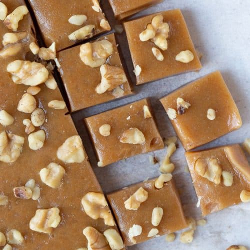caramels topped with chopped walnuts on white parchment paper.