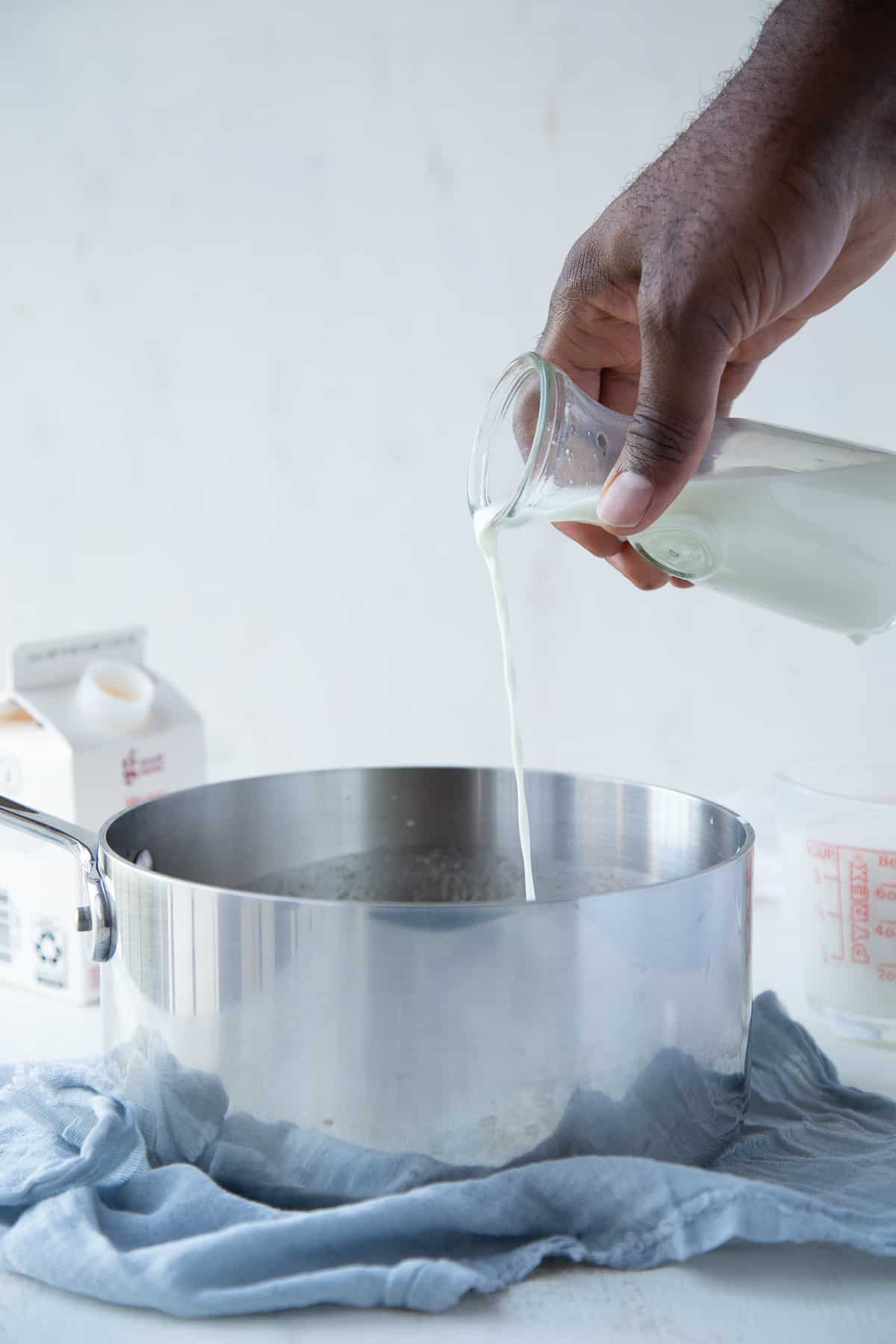 hand pouring heavy cream into a saucepan sitting on a blue tea towel.