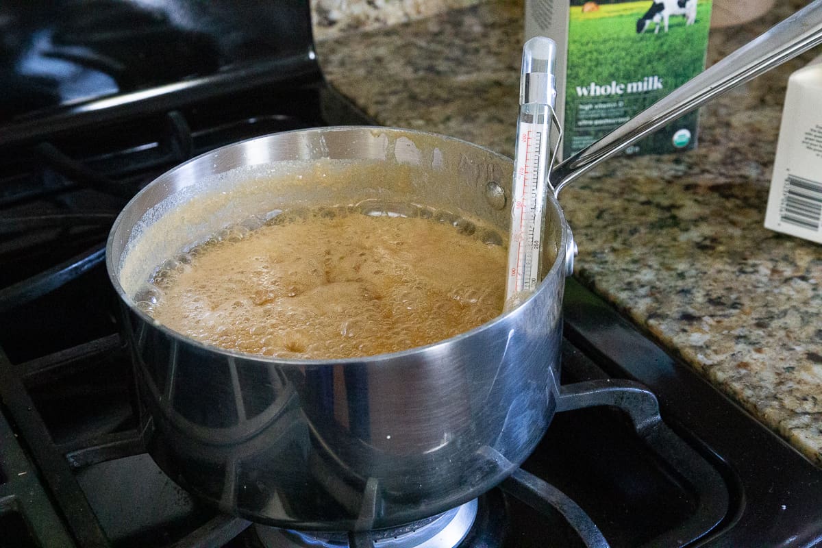 pot of caramel bubbling on the stove with a candy thermometer in the pot.