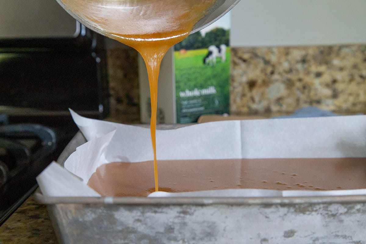 hand pouring caramel into a metal pan lined with parchment paper.