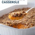 hand lifting spoon of sweet potato casserole out of white casserole dish.