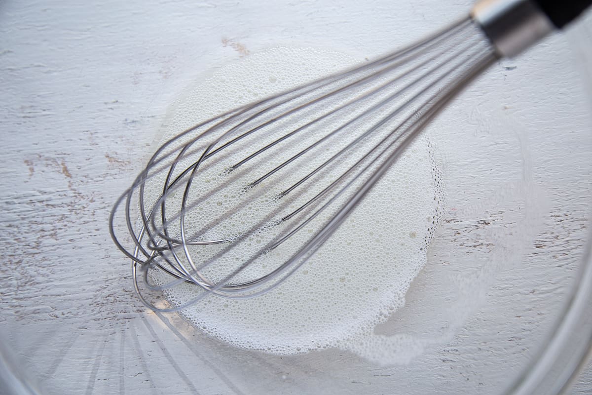 whisk in a bowl with a foamy egg white.