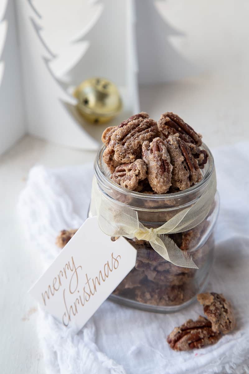glass jar of roasted pecans with a gold ribbon and merry christmas gift tag.