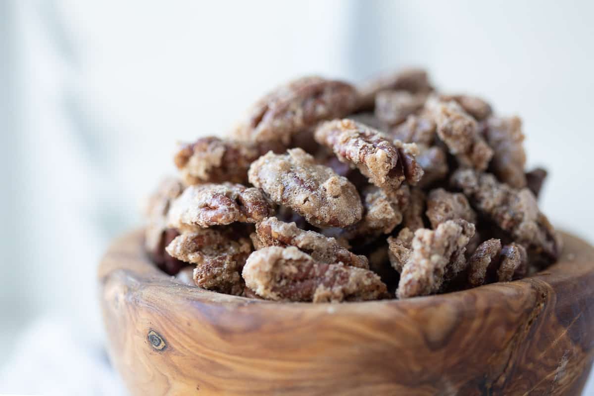 cinnamon roasted nuts in a wooden bowl with white wooden christmas trees in the background.