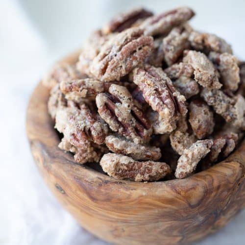 cinnamon roasted pecans in a wooden bowl on a white table.